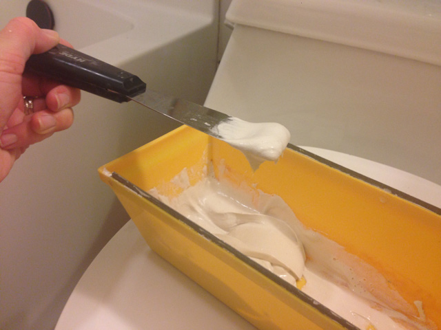 putty knife holding drywall mud over yellow drywall tray sitting on toilet