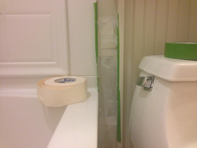 green painter's tape sitting on toilet, drywall paper tape sitting on bathtub, drywall repair with mud and tape in place