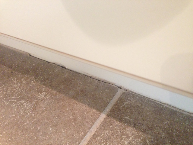 brown kitchen tile with missing grout next to cream cabinets