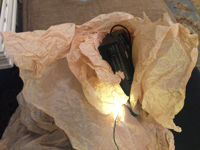 black box from battery-powered Christmas light wrapped in tan tissue paper
