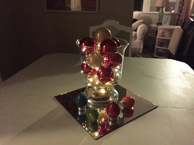 glass vase filled with ornaments and lights set on white dining table with mirror tile