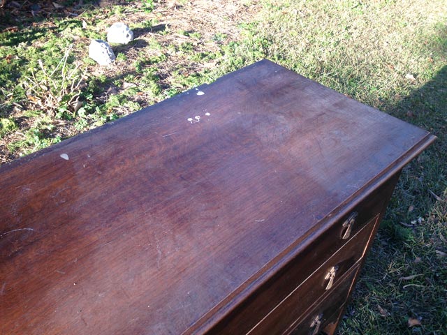 top of stained wood dresser with paint splotch and dust sitting in grass