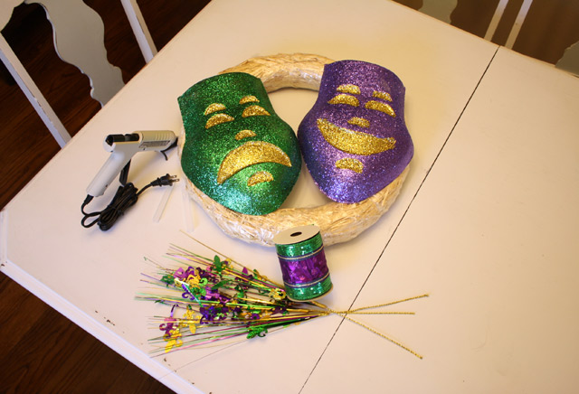 Mardi Gras masks on straw wreath form on white dining table with hot glue gun and purple gold and green ribbon